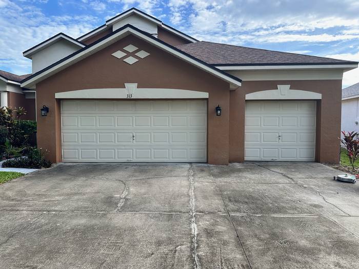 Concrete driveway before pressure washing at a three-car garage, stained and darkened along the expansion joints, Central Florida
