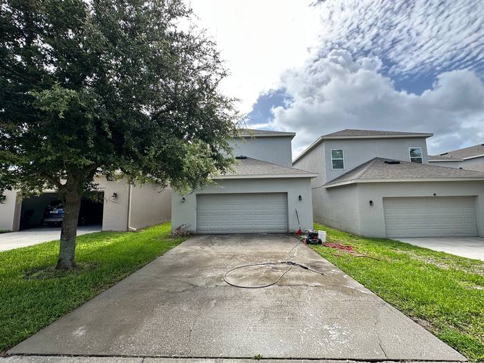 Concrete driveway before pressure washing in front of a two-story stucco home, grey with mildew, Central Florida